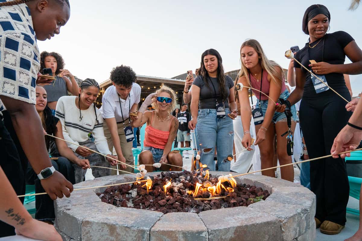 Group of guests roasting marshmallows around a beachside fire pit during an outdoor waterfront event