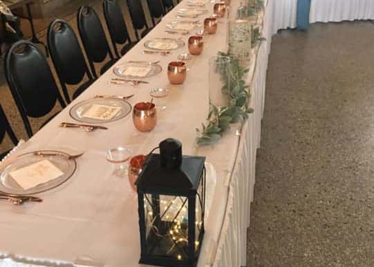A long table and chairs set with linens and lantern centerpieces