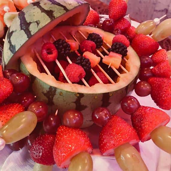 Various berries displayed inside of a cut-open watermelon on a buffet table 