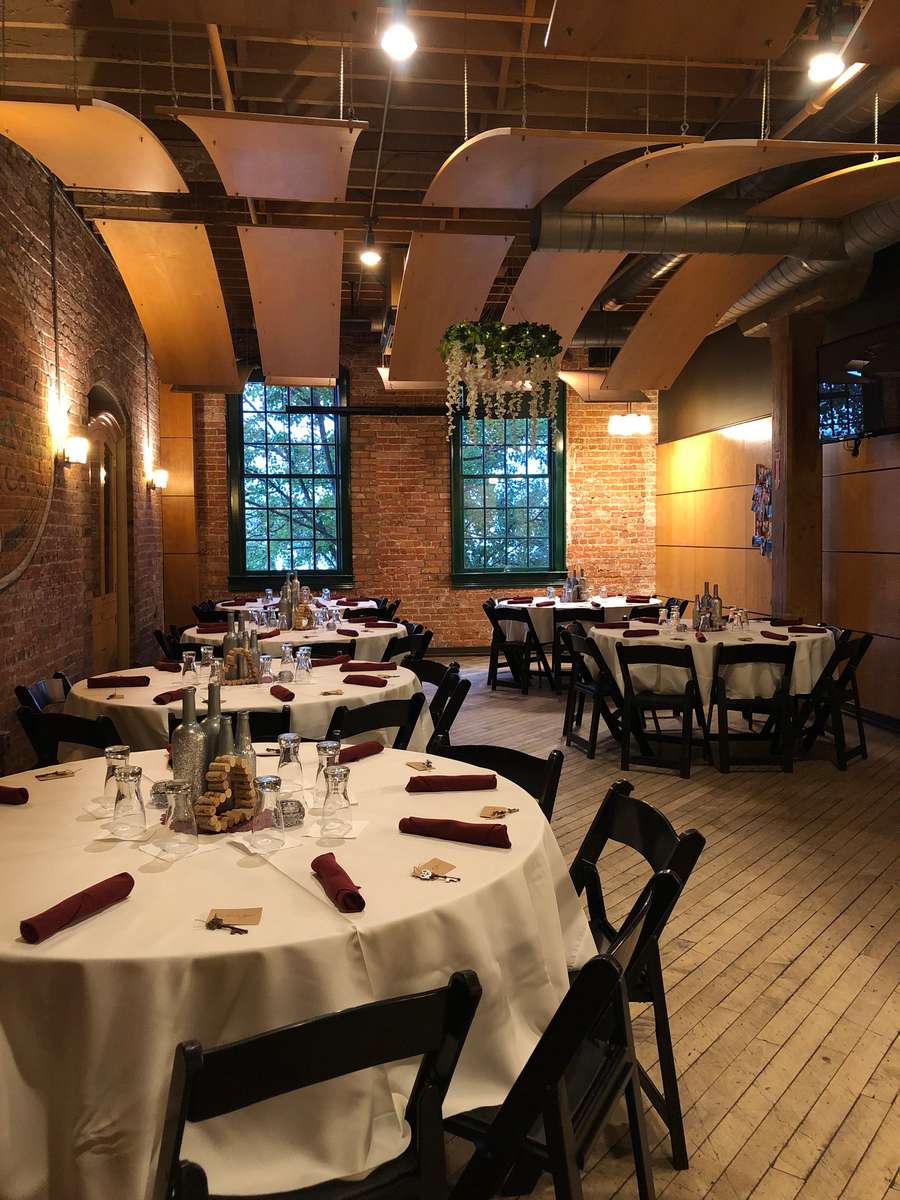 Photograph of the Lazy Daze Lounge in Downtown Rochester, Michigan. Round tables with white linen, red rolled silverware, flowers as center pieces, and exposed brick. Private event room for weddings, wedding rehearsals, birthdays, anniversaries, and more.