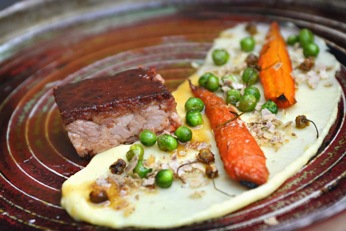 Delicious gourmet dish featuring braised pork belly, carrots, peas, and puree. Perfect for culinary presentations.