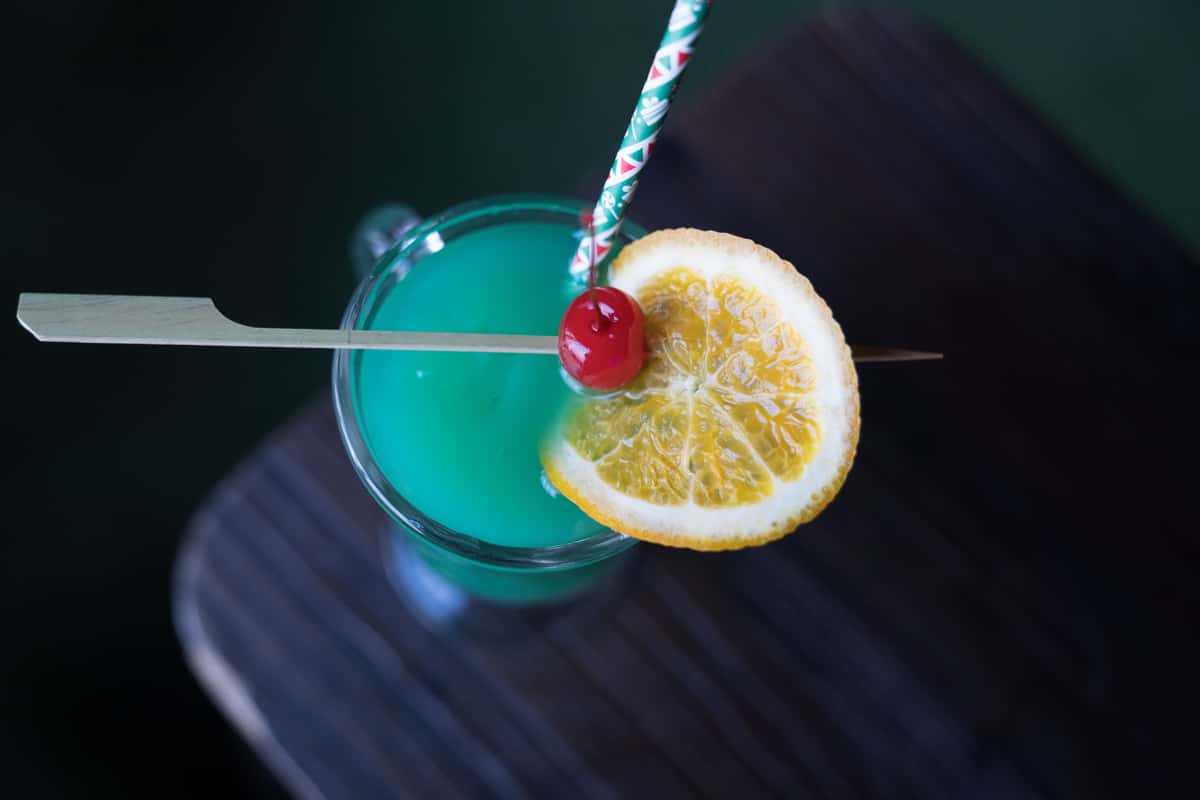 green cocktail beverage with citrus and cherry garnish