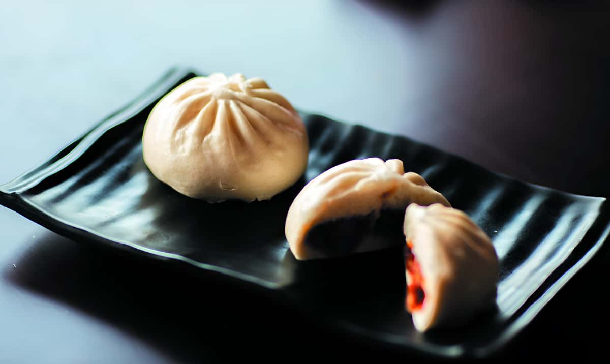 Steamed Asian buns with savory filling served on a black ceramic plate