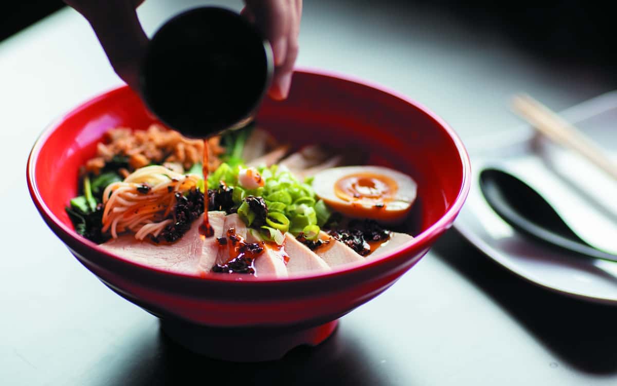 Japanese ramen bowl with sliced pork, soft-boiled egg, green onions, noodles, and savory sauce