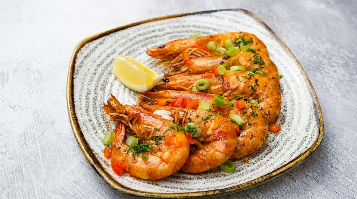 Grilled shrimp served on a grey plate with a lemon wedge and garnished with chopped scallions and red bell pepper.