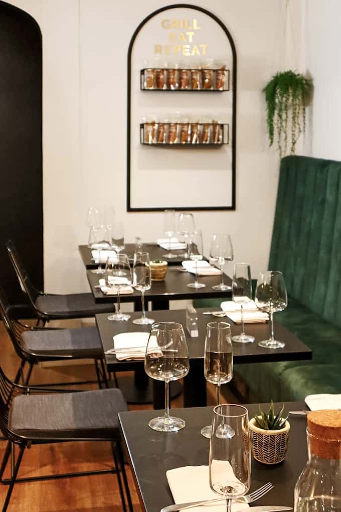 Modern restaurant interior with neatly set dining tables, wine glasses, and cozy booth seating under minimalist wall decor