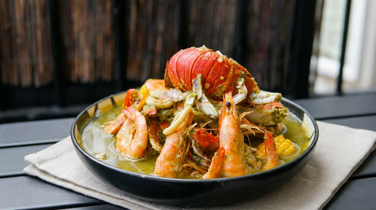 Seafood dish in green curry sauce, featuring full prawns, crab claws, squid rings, and half a red lobster tail.