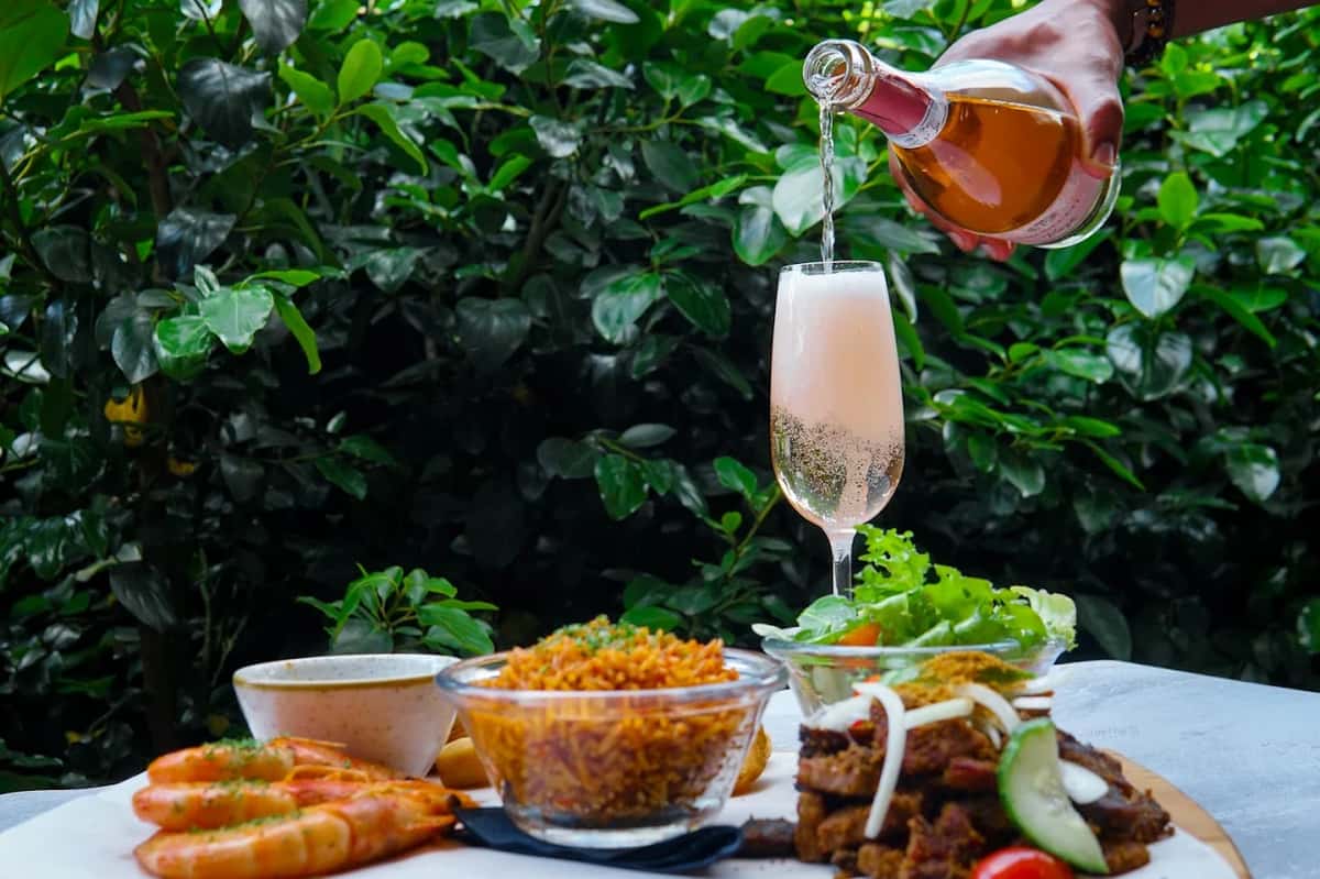 tropical cocktail being poured into a glass beside a spread of fried appetizers and sides in an outdoor garden setting