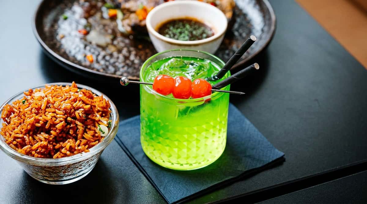 Lime green cocktail garnished with three red cherries and black straws.