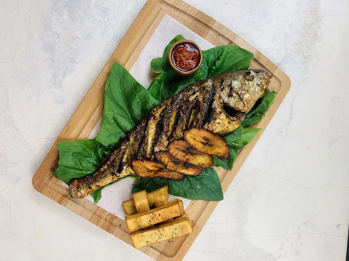 grilled whole fish served with roasted potatoes and greens on a wooden board in a coastal restaurant