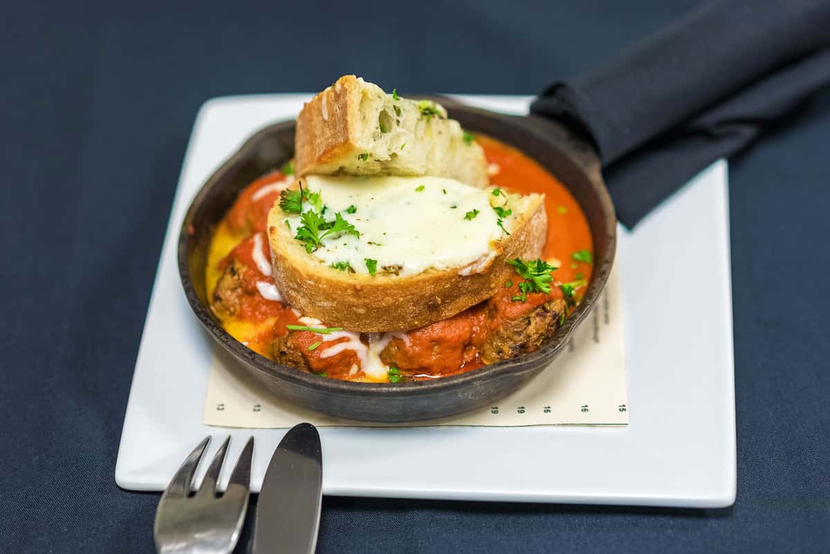 A rich and comforting seafood stew is served in a skillet, filled with a vibrant tomato-based broth and tender seafood. Topped with a perfectly poached egg and a slice of toasted bread, the dish is garnished with fresh herbs for a rustic, flavorful presentation that feels both hearty and refined.