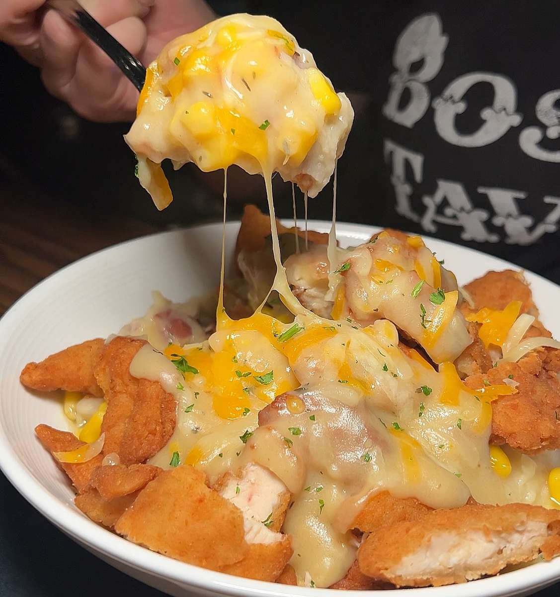 Close-up of crispy fried chicken bites smothered in melted cheddar and white cheese with savory gravy, featuring a gooey cheese pull in a white bowl.