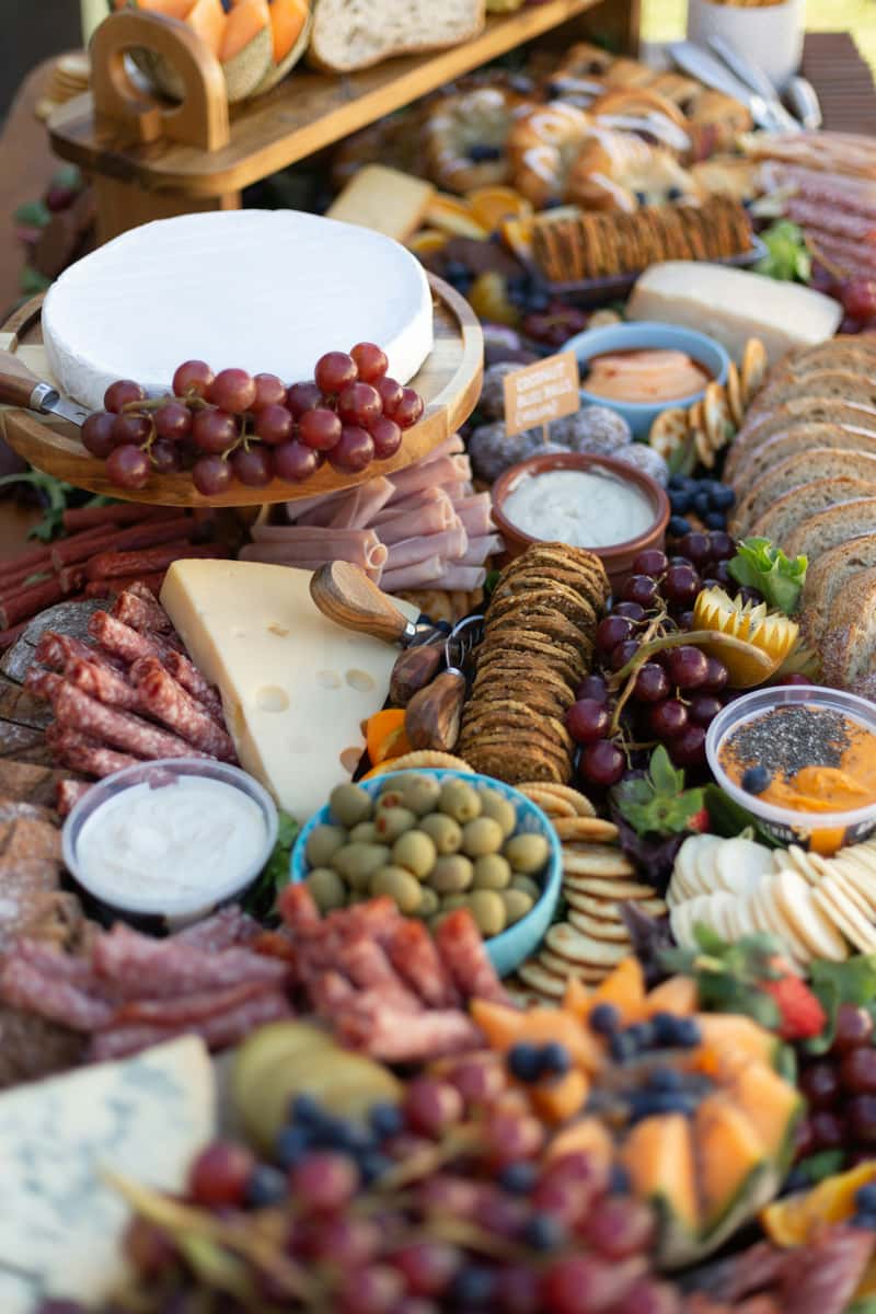 Lush grazing table filled with an assortment of cheeses, green olives, crackers, dips, cold cuts, and fresh grapes, styled for a gourmet party platter or upscale picnic spread.