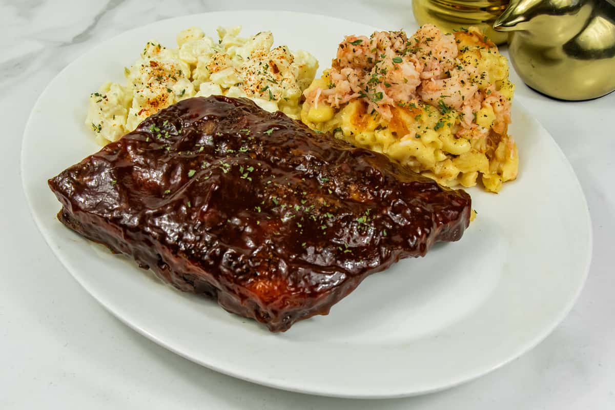 Barbecue ribs served with creamy macaroni and cheese topped with salmon and a side of seasoned potato salad.