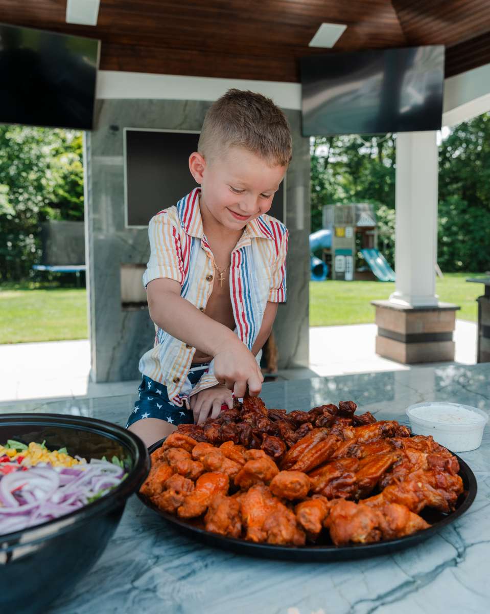 Child grabbing chicken from a wing tray