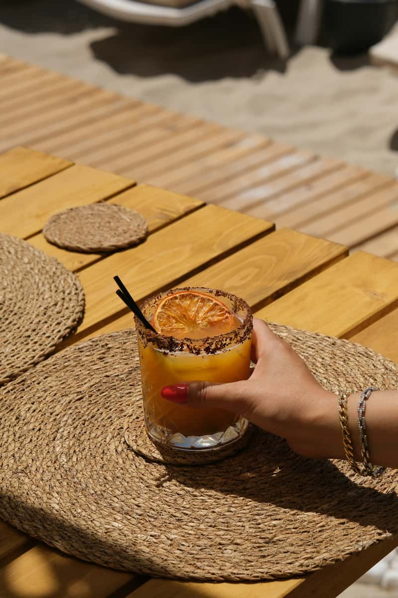 Cocktail in hand on a wooden table by the beach