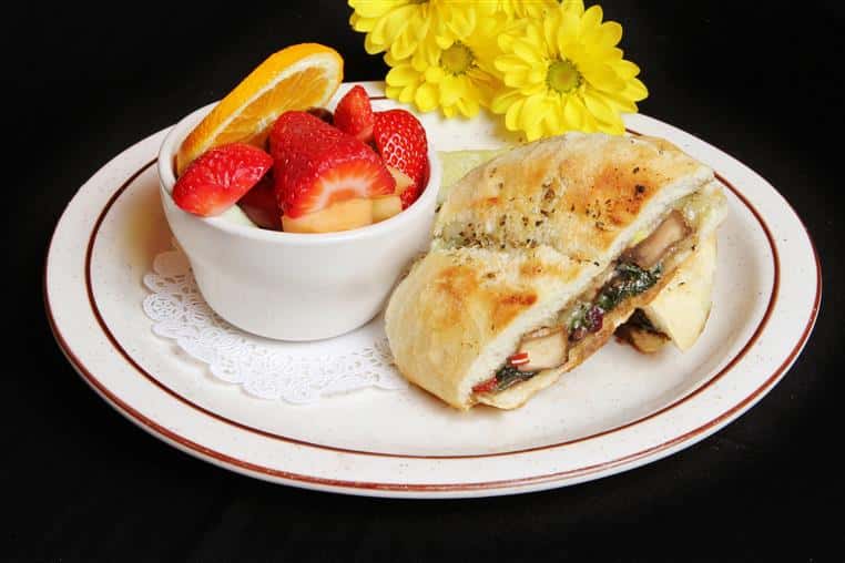 Grilled chicken panini with sliced strawberries and oranges in a bowl