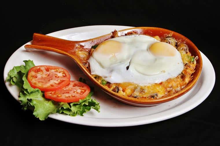 Breakfast skillet with two fried eggs on top with sliced tomatoes and lettuce
