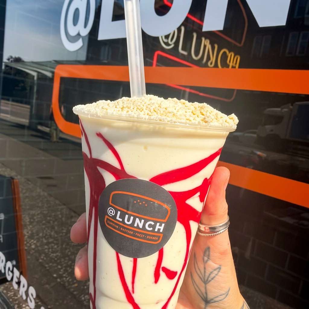 @Lunch creamy milkshake with red fruit sauce swirls and a crumb topping in a branded takeaway cup
