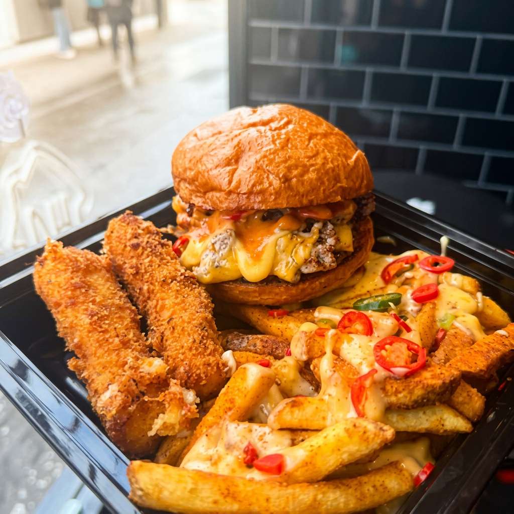 Loaded cheeseburger with crispy chicken tenders and cheesy seasoned fries topped with sliced peppers