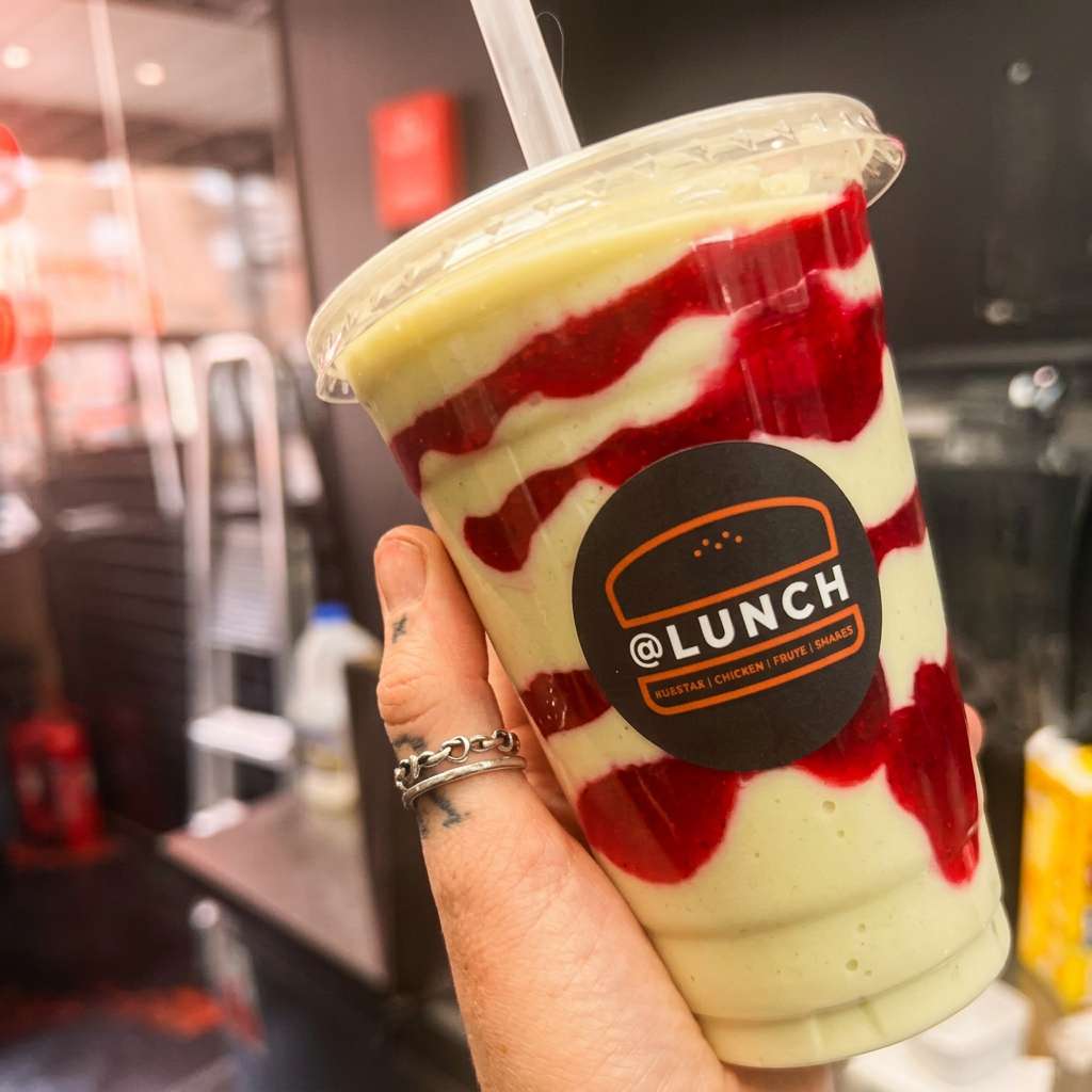 @Lunch creamy milkshake with vibrant red fruit sauce swirls served in a branded takeaway cup
