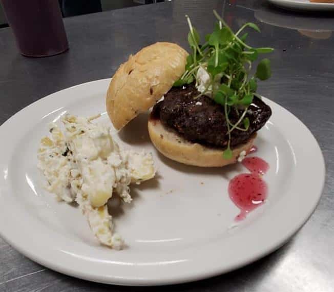burger topped with micro greens served with a side of potatoes