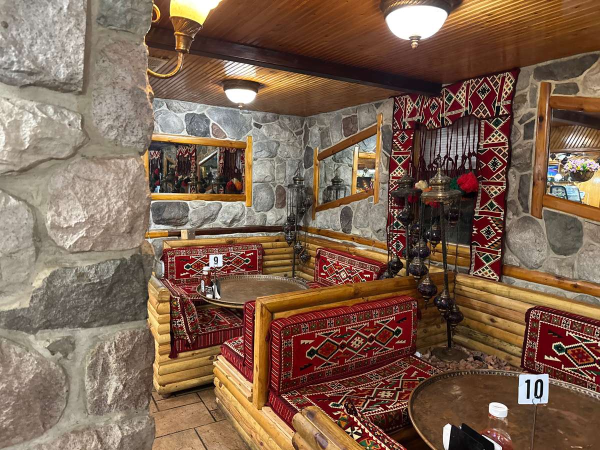 Rustic Mediterranean restaurant seating with log benches, red patterned cushions, stone walls, and ornate hanging lanterns.