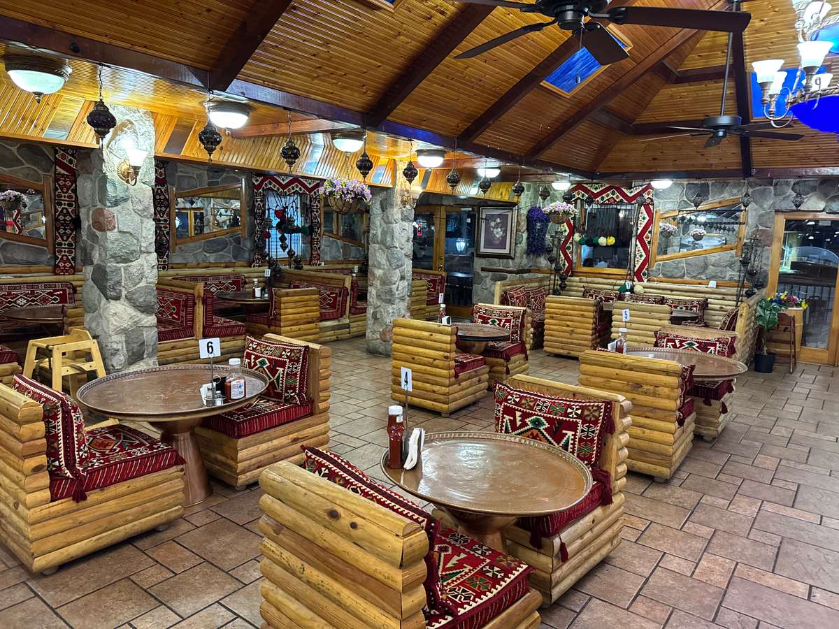 Cozy Mediterranean restaurant interior with wooden log seating, vibrant red patterned cushions, and colorful hanging mosaic lamps.