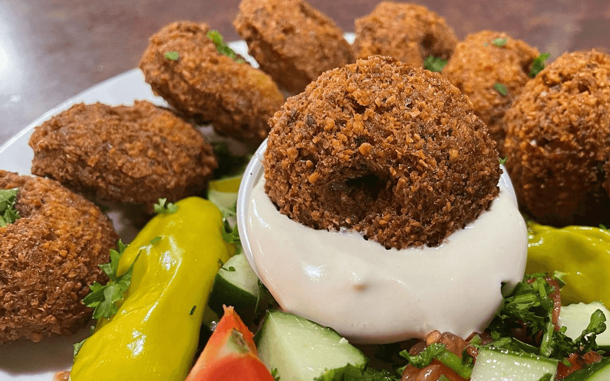 Crispy falafel served with creamy tahini sauce, fresh cucumber, tomatoes, parsley, and pickled peppers for a Mediterranean flavor.