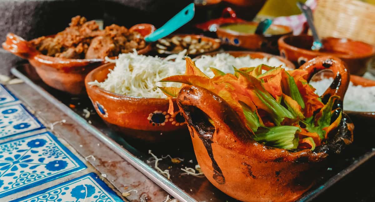 Rustic Mexican dishes served in clay bowls with shredded cabbage and traditional sides—warm, authentic Mexican kitchen presentation.