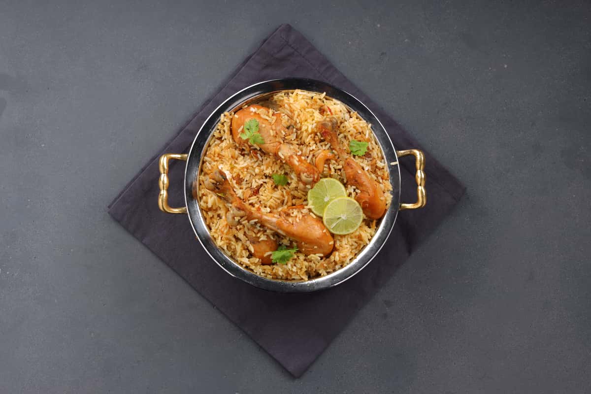 Spiced chicken biryani served in a metal pot with rice, herbs, and visible chicken pieces.