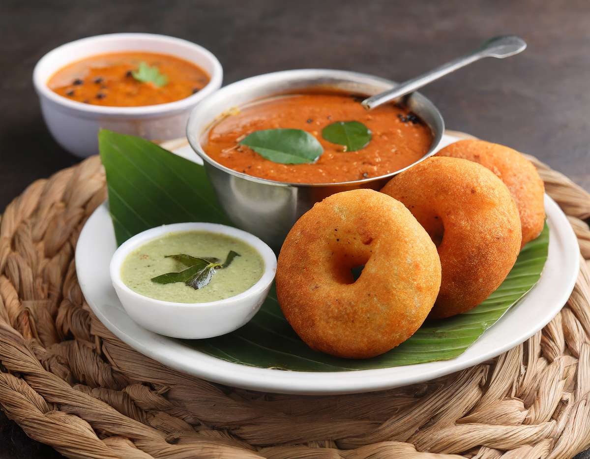 Traditional South Indian vada served with chutneys and sambar on a plate.
