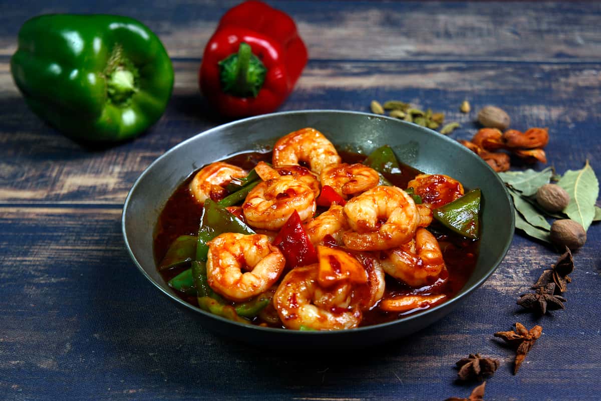 Prawns cooked in a spicy green pepper sauce, served in a dark bowl with vegetables.