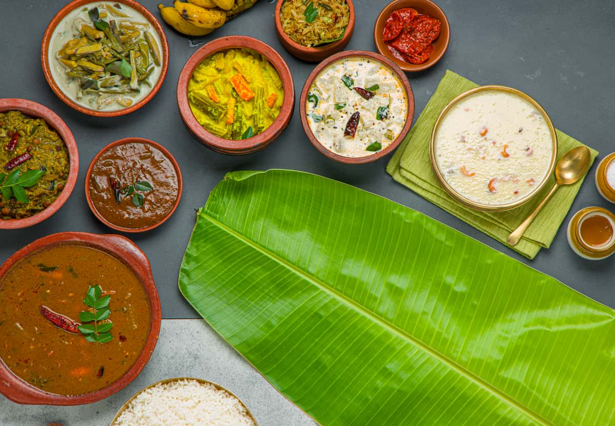 Traditional South Indian Kerala meal served on a banana leaf with rice and assorted vegetable curries in small bowls.
