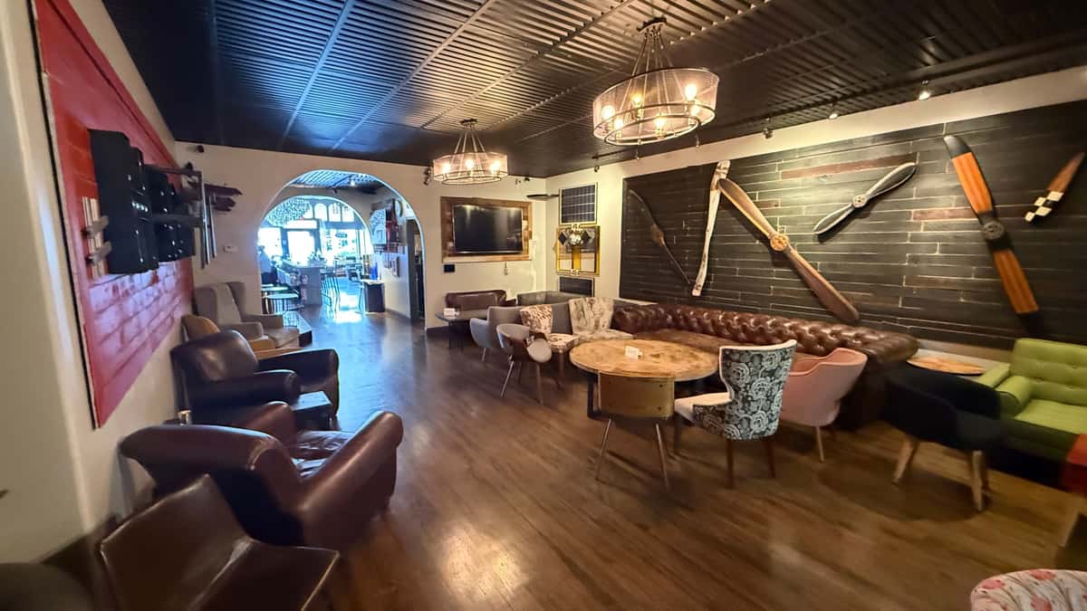 Cozy lounge with leather chairs, patterned seating, and wooden tables, featuring airplane propellers mounted on a dark wall.