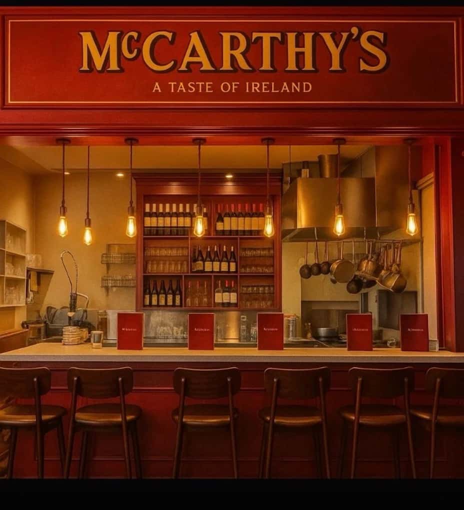 Bright red McCarthy's – A Taste of Ireland restaurant bar with warm pendant lighting, bar stools along the counter, and an open kitchen with copper pots and shelves of wine bottles