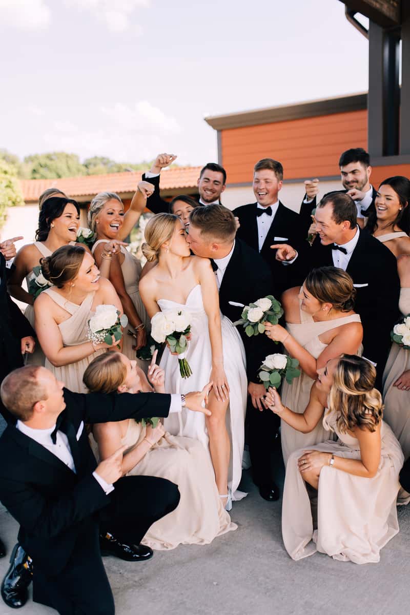 Picture of bride and groom kissing with wedding party around them.