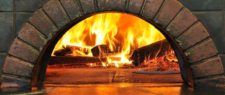Wood burning oven with pieces of wood on fire with a thin crust pizza being cooked