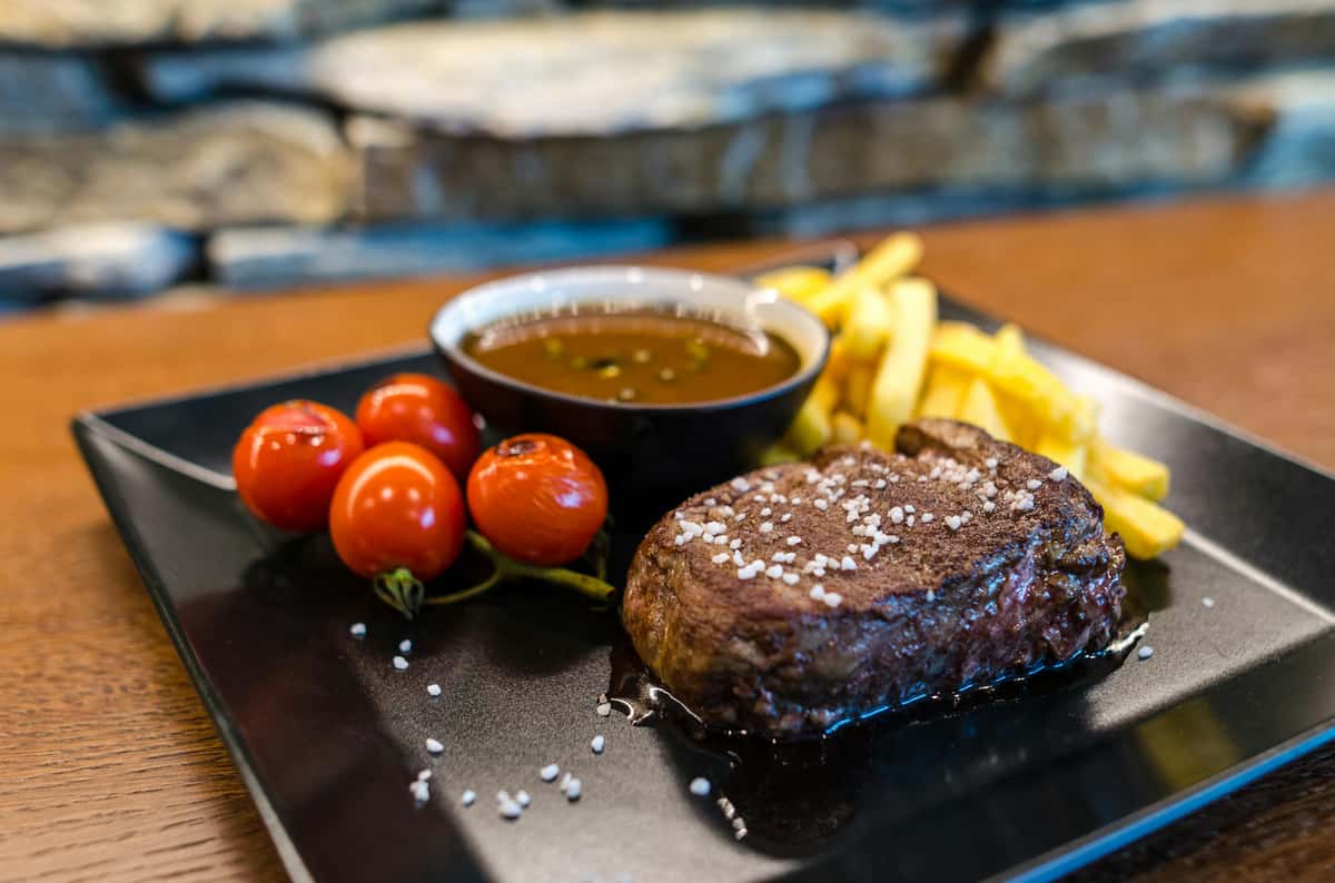 Delicious steak dinner with fries, cherry tomatoes, and sauce served at City Limits Bar & Grill.