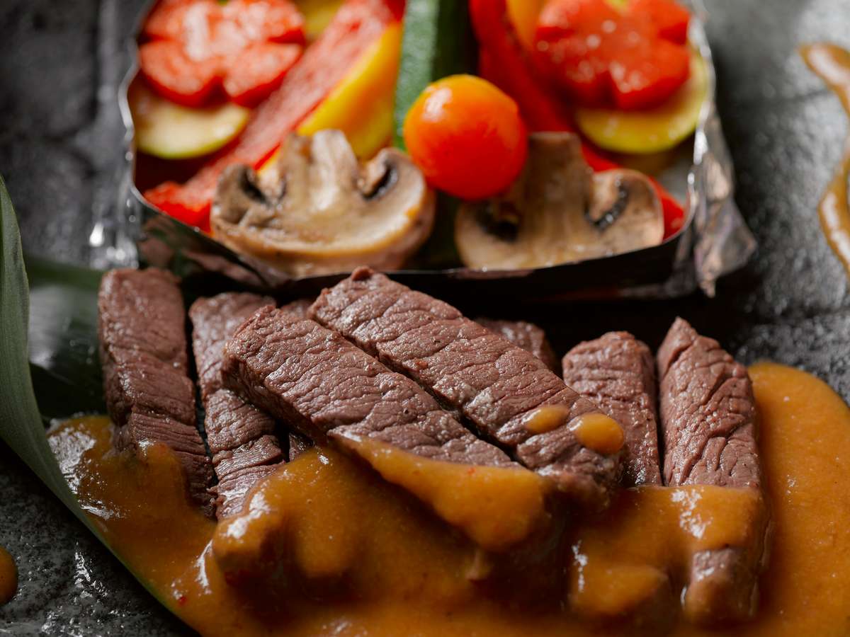 Close-up of sliced steak with sauce and colorful grilled vegetables from City Limits Bar and Grill.