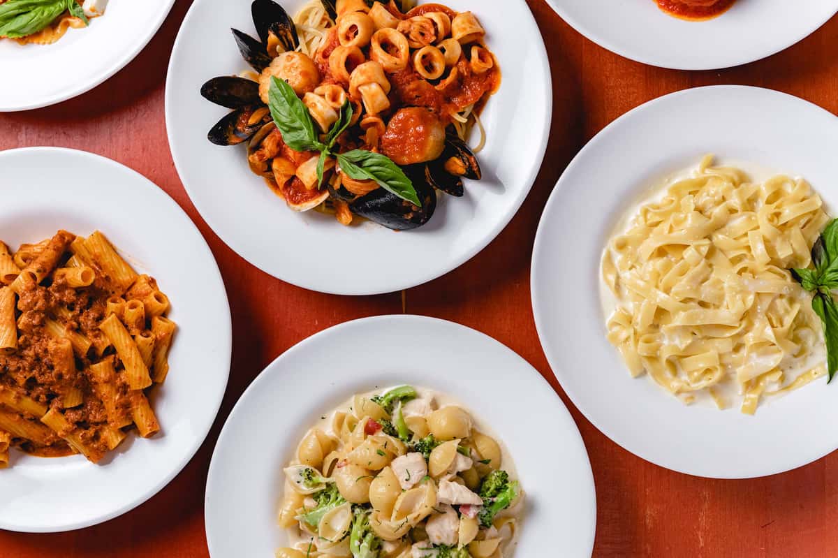 Assortment of freshly prepared Italian pasta dishes at Pasta Lovers Trattoria in Midtown Manhattan, NYC, featuring seafood pasta with mussels and tomato sauce, creamy fettuccine, and pasta with vegetables and fresh herbs.