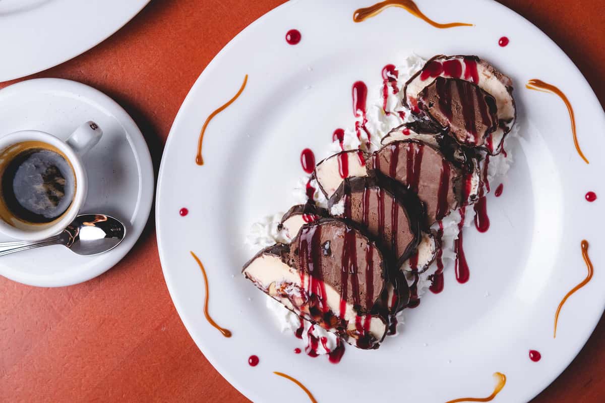 Rich chocolate dessert topped with vanilla ice cream and drizzled with chocolate and raspberry sauces, served on a white plate with decorative sauce swirls at Pasta Lovers Trattoria in Midtown Manhattan, NYC.