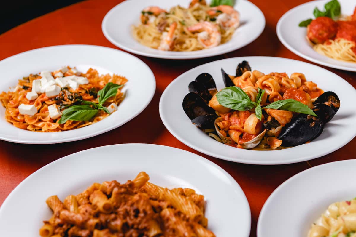 Assortment of freshly prepared Italian pasta dishes at Pasta Lovers Trattoria in Midtown Manhattan, NYC, featuring pasta with tomato sauce, seafood, vegetables, and fresh herbs served on white plates.