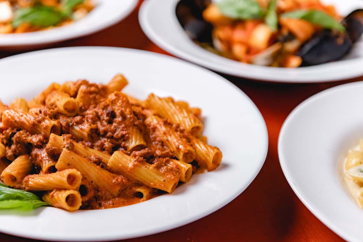 Rigatoni pasta tossed in a rich tomato and meat sauce, garnished with fresh herbs and served on a white plate at Pasta Lovers Trattoria in Midtown Manhattan, NYC.