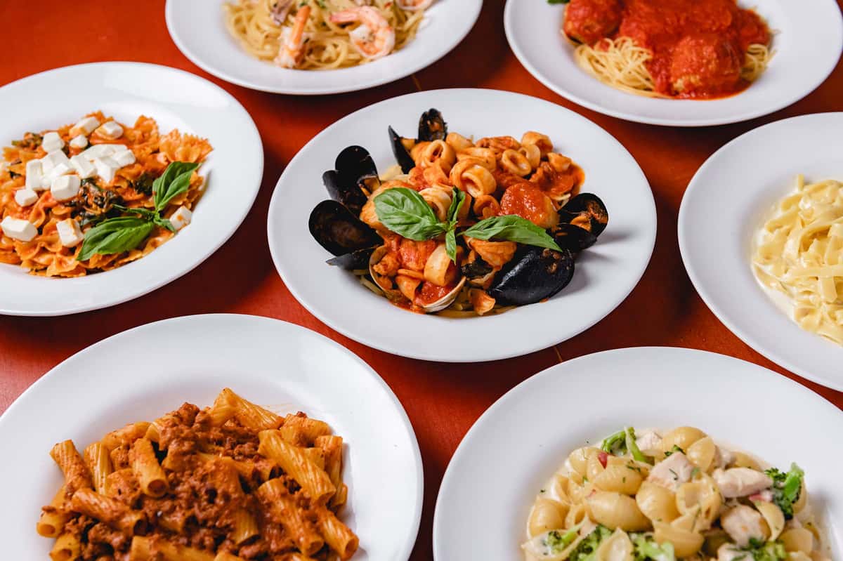 Assortment of freshly prepared Italian pasta and seafood dishes at Pasta Lovers Trattoria in Midtown Manhattan, NYC, featuring mussels, pasta with tomato sauce, fresh vegetables, and classic Italian specialties served on white plates.