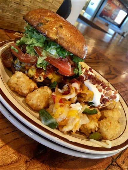 burger on a bun topped with lettuce, tomato and cheese served with tater tots