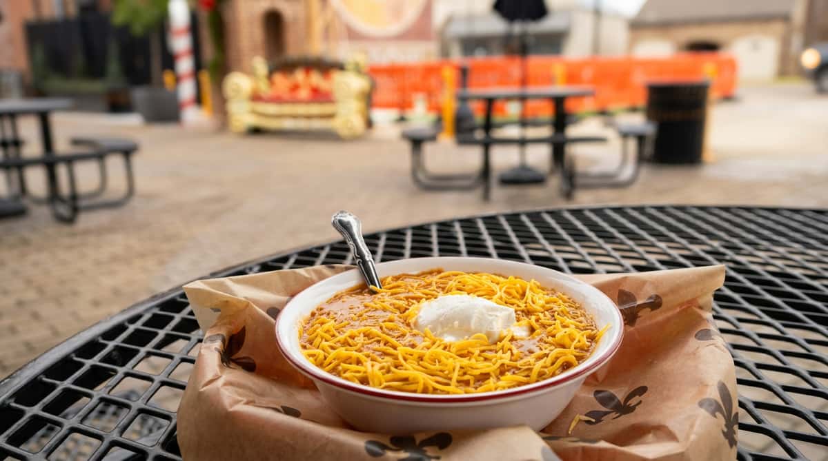 Hearty bowl of chili topped with shredded cheddar cheese and a dollop of sour cream, served on an outdoor café patio in a cozy downtown setting.