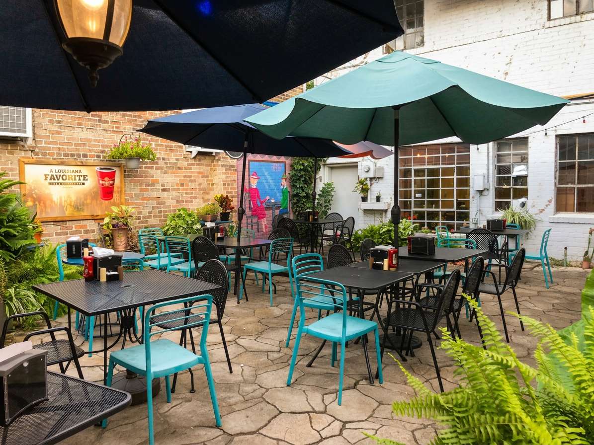 Outdoor patio dining area with black tables, teal chairs, large umbrellas, and brick walls.