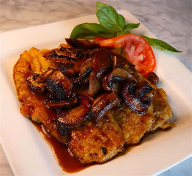 chicken marsala with mushrooms on top and a tomato on the side
