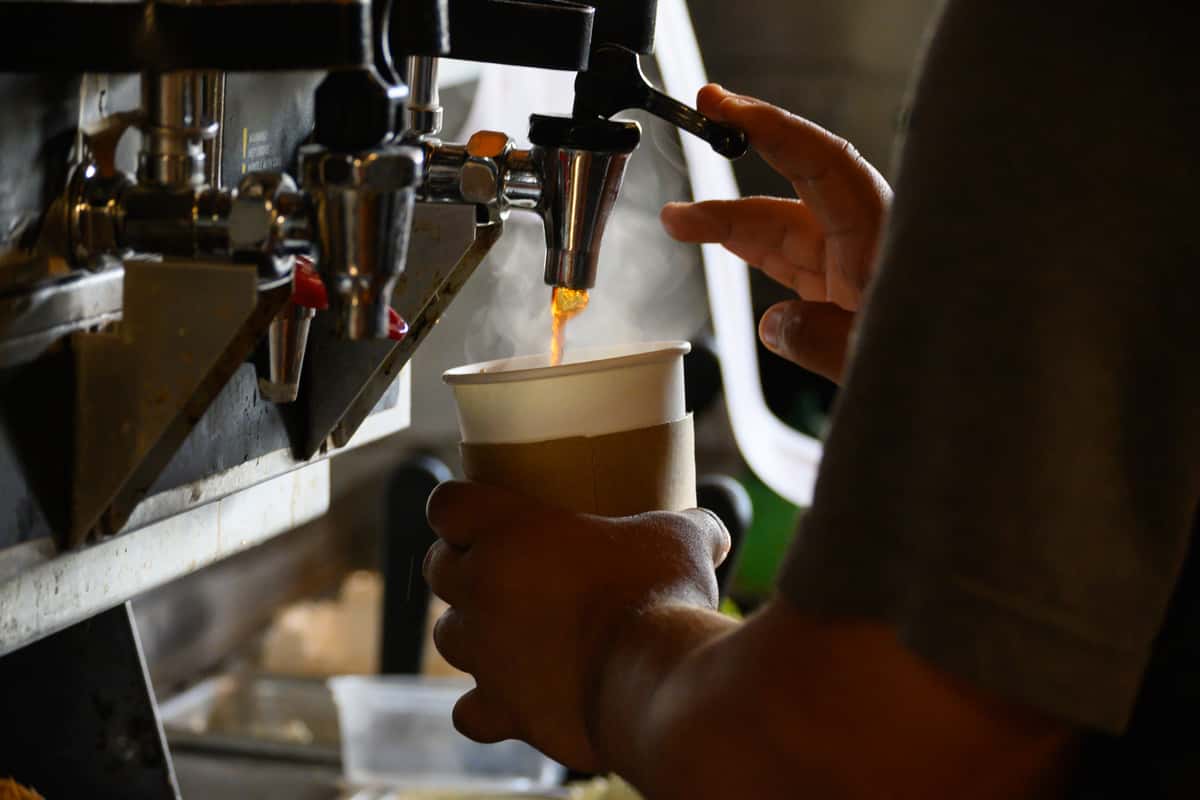 Fresh coffee pouring from a commercial brewer into a takeaway cup at a busy coffee shop